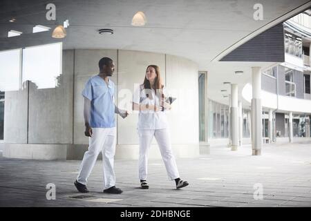 Die gesamte Länge der selbstbewussten Krankenschwestern diskutieren, während Sie auf dem Fußweg gehen Im Krankenhaus durch Glas gesehen Stockfoto