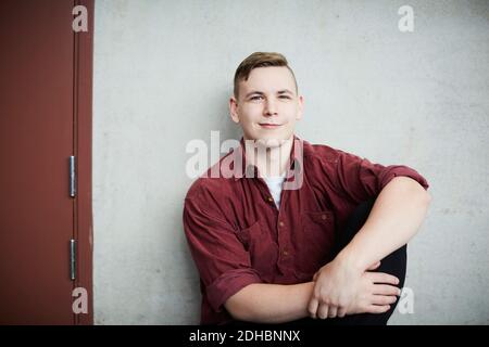 Portrait eines jungen Studenten, der an der Wand in der Universität sitzt Stockfoto
