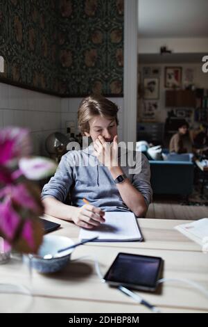 Teenager Junge Hausaufgaben machen, während am Tisch sitzen Stockfoto