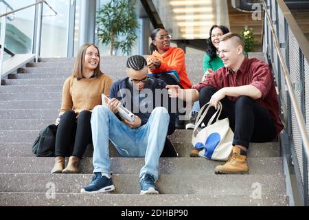 Low-Angle-Ansicht von glücklichen männlichen und weiblichen Freunden sprechen Während der Sitzung auf der Treppe an der Universität Stockfoto