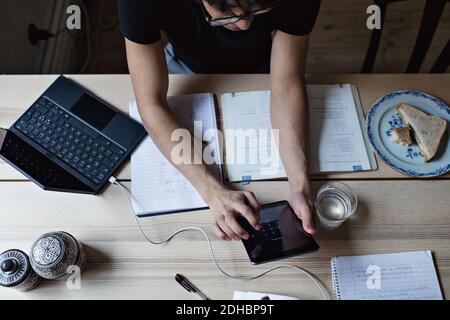 High-Angle-Ansicht von studious jungen Mann mit digitalen Tablet Während der Hausaufgaben am Tisch Stockfoto
