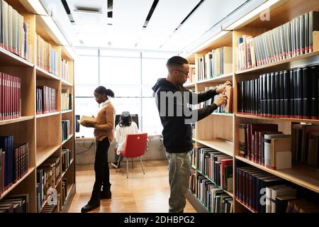 Studenten suchen Buch, während Frau mit Computer in der Bibliothek an universität Stockfoto