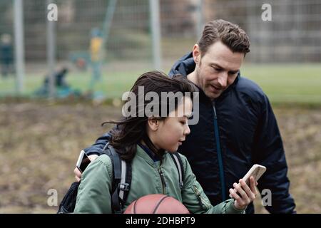 Sohn zeigt seinem Vater sein Smartphone, während er bei ihm steht Sportplatz Stockfoto