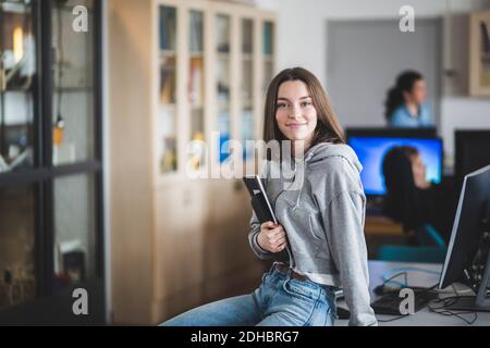 Portrait der lächelnden High School Schülerin sitzt mit Büchern Auf dem Schreibtisch im Klassenzimmer Stockfoto