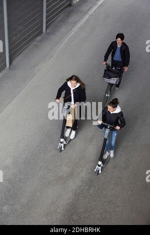 High-Angle-Ansicht von männlichen und weiblichen Freunden Reiten elektrisch Roller und Fahrrad auf der Straße in der Stadt Stockfoto