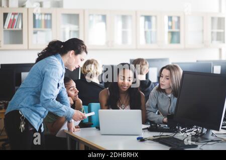 Ältere Lehrerin, die weiblichen Schülern mit Laptop im Computerlabor hilft In der High School Stockfoto