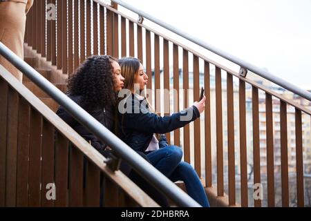 Teenage-Mädchen, die Selfie mit weiblichen Freund, während sitzend auf Treppe Stockfoto