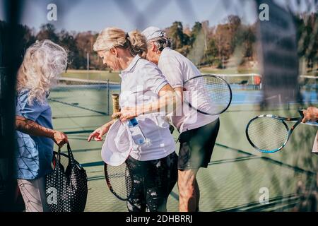 Ältere männliche und weibliche Freunde mit Schlägern und Tasche reden Beim Stehen auf dem Tennisplatz Stockfoto