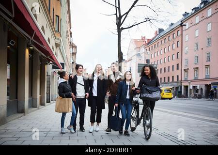 Lächelnde männliche und weibliche Teenager-Freunde, die auf dem Bürgersteig hereinlaufen Stadt Stockfoto