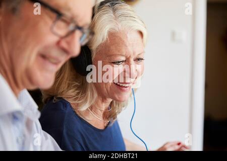 Lächelnde ältere Frau, die Kopfhörer trägt, von einem Mann zu Hause Stockfoto