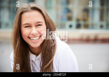 Porträt von lächelndem Teenager-Mädchen im Schulhof sitzen Stockfoto