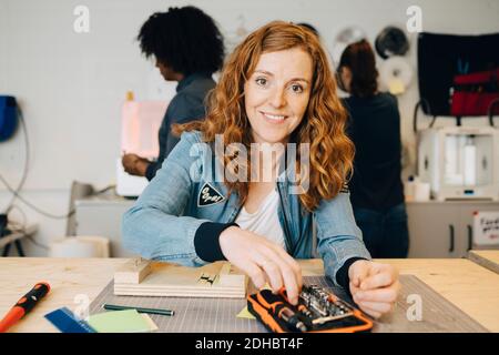 Portrait einer lächelnden Rothaarerin, die an der Werkbank sitzt Kollegen, die im Kreativbüro arbeiten Stockfoto