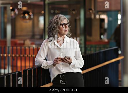 Erwägen, eine Geschäftsfrau mit einem Smartphone zu benutzen, während sie am Geländer steht Im Büro Stockfoto