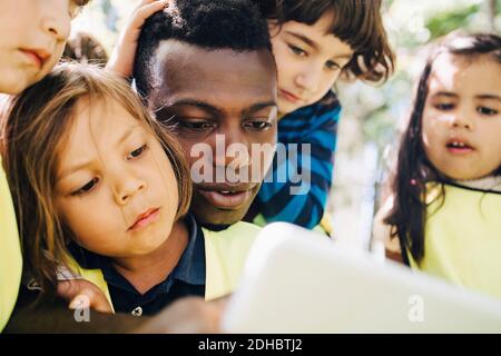 Männlicher Lehrer, der digitale Tablette mit Schülern auf dem Spielplatz teilt Stockfoto