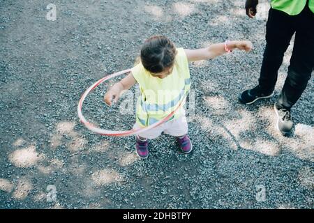 High-Winkel-Ansicht von Mädchen spielen mit Kunststoff-Reifen durch Männlicher Lehrer auf dem Spielplatz Stockfoto