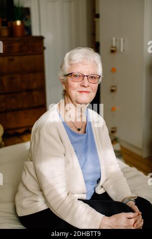 Porträt einer lächelnden Rentnerin im Ruhestand, die auf dem Bett sitzt Pflegeheim Stockfoto