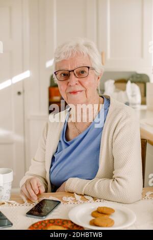 Porträt einer älteren Frau im Ruhestand, die mit einem Smartphone sitzt Tabelle im Pflegeheim Stockfoto