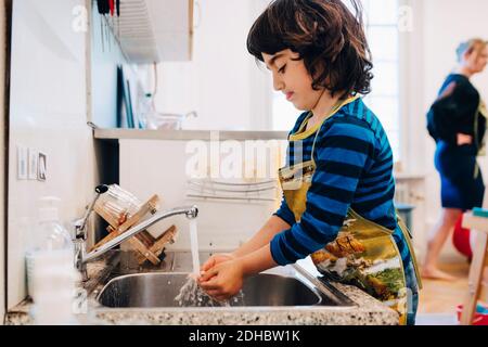 Seitenansicht des Jungen, der die Hände unter dem Wasserhahn im Waschbecken wascht Bei der Kinderbetreuung Stockfoto