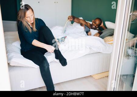 Frau am Telefon sprechen, während sich mit Mann und Tochter liegt im Hintergrund auf dem Bett Stockfoto