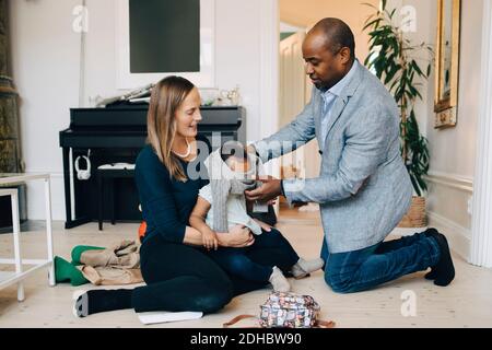 Eltern kleiden Mädchen, während auf dem Boden im Wohnzimmer sitzen Zu Hause Stockfoto