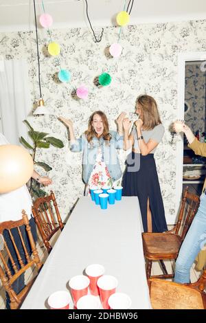 Überrascht junge Frau spielt Bier Pong mit Freunden während des Abendessens Party zu Hause Stockfoto