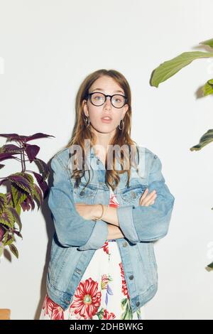 Porträt einer jungen Frau, die mit gekreuzten Armen gegen Weiß steht Wand zu Hause Stockfoto