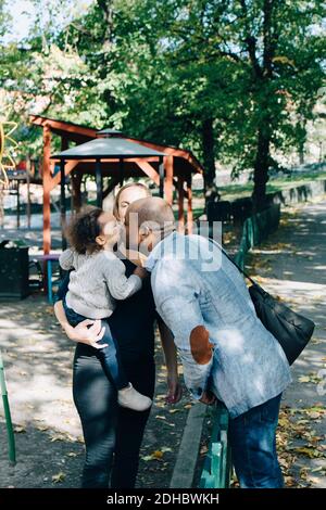 Vater küsst Tochter, während Mutter trägt sie im Park Stockfoto