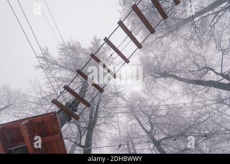 Leere Adrenalin Seil Spielplatz in Baumstämmen in nebligen und Nebliger Winterwald Stockfoto