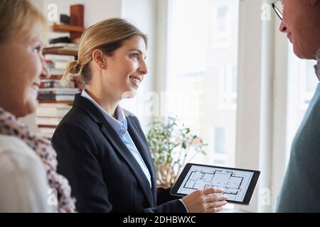 Lächelnd Immobilienmakler zeigt Blaupause des neuen Hauses auf Digitales Tablet zum Koppeln Stockfoto