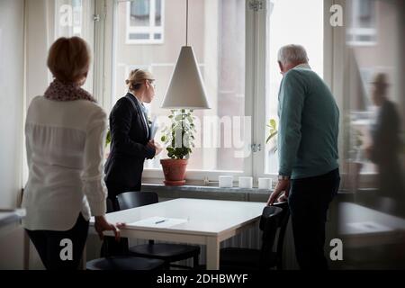 Seniorenpaar und Immobilienmakler, die durch Fenster schauen Neues Zuhause Stockfoto