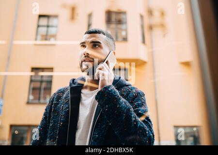 Low-Winkel-Ansicht des selbstbewussten jungen Geschäftsmann im Gespräch auf smart Telefon durch Fenster gesehen Stockfoto