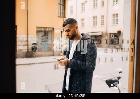 Selbstbewusster junger Geschäftsmann mit Smartphone durch Fenster gesehen Stockfoto