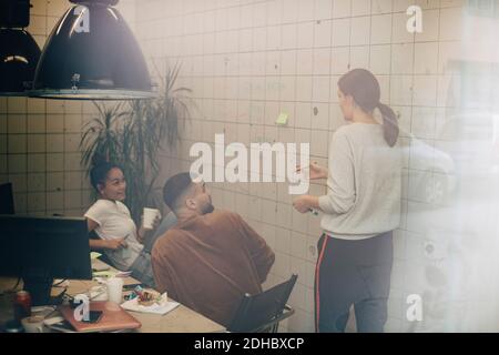 Multi-ethnische Computer-Programmierer diskutieren über Wand bei kreativen Büro gesehen Durchgangsfenster Stockfoto