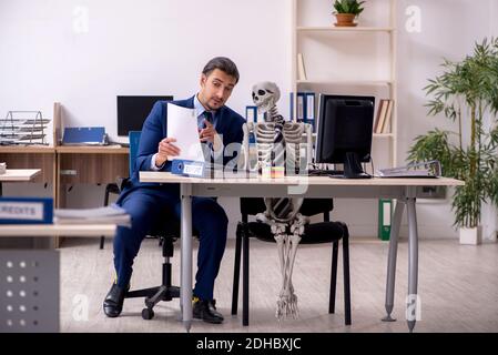 Junger männlicher Angestellter mit Skeletten im Büro Stockfoto