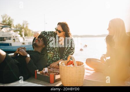 Freunde, die Kirschen genießen, während sie am Steg gegen den See sitzen Sommer Stockfoto