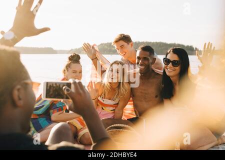 Mann fotografiert glückliche Freunde auf Smartphone am Steg in Sommer Stockfoto