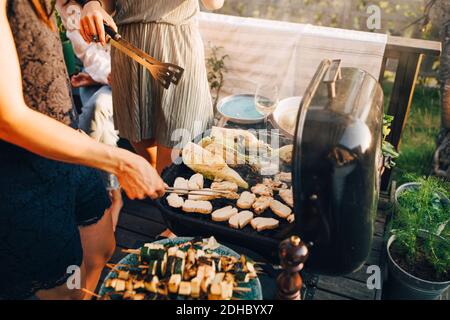 Mittelteil der weiblichen Freunde Grillen Essen auf Grill bei Hof Stockfoto