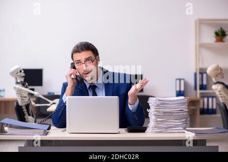 Junger männlicher Angestellter mit Skeletten im Büro Stockfoto