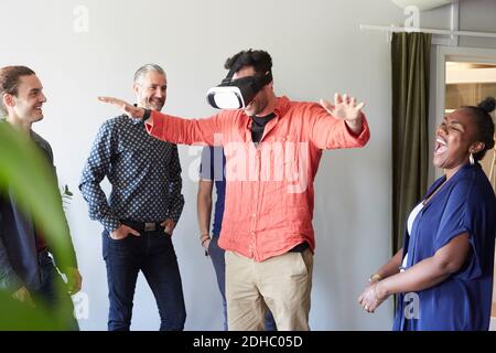 Glückliche Geschäftsleute, die männliche Kollegen mit Virtual Reality betrachten Simulator im Büro Stockfoto