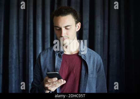 Kreativer Geschäftsmann mit Smartphone gegen Vorhang im Büro Stockfoto