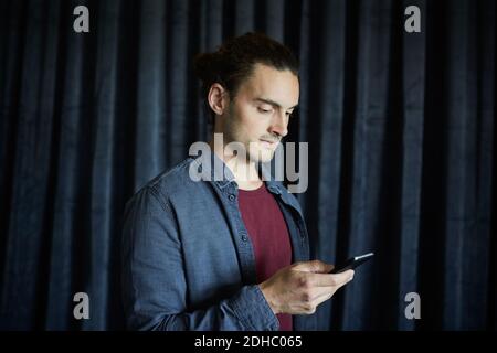 Kreative Geschäftsmann mit Handy gegen Vorhang im Büro Stockfoto