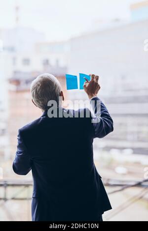 Rückansicht des Geschäftsmannes, der Klebehinweise auf das Fensterglas klebt Bei der Strategieplanung im Kreativbüro Stockfoto