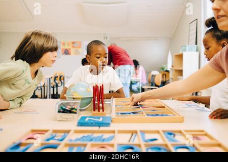 Schüler lernen Schreibweisen am Tisch von Lehrer im Klassenzimmer Stockfoto