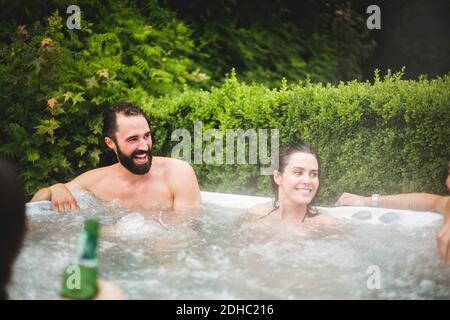 Fröhliche männliche und weibliche Freunde, die wegschauen, während sie in genießen Wannen-Whirlpool Stockfoto