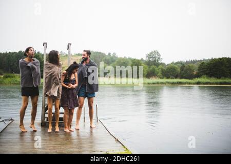 Freunde wickelten sich in Handtücher und unterhielten sich, während sie auf dem Steg standen see gegen klaren Himmel Stockfoto