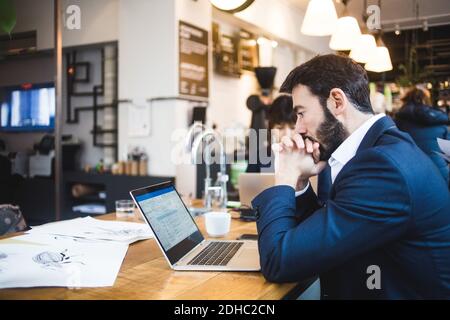 Seitenansicht des selbstbewussten männlichen professionellen Blick auf Laptop auf Tisch im Büro Stockfoto