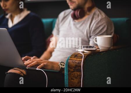 Mittelteil des Geschäftsmannes mit Laptop sitzend durch weibliche Kollegin auf Sofa im kreativen Büro Stockfoto