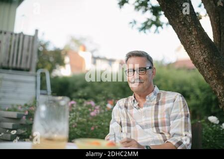 Porträt eines lächelnden älteren Mannes, der am Tisch im Hinterhof sitzt Stockfoto