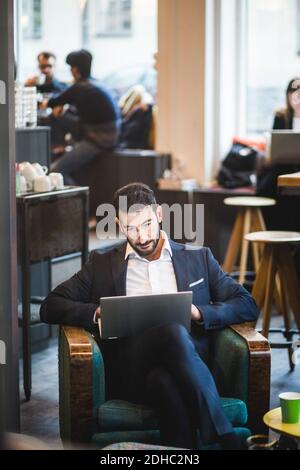 Selbstbewusster Geschäftsmann mit Laptop auf Stuhl im kreativen Büro sitzen Stockfoto