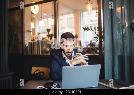 Selbstbewusster Geschäftsmann mit zusammengekrallten Händen und Blick auf den Laptop auf dem Schreibtisch Im kreativen Büro